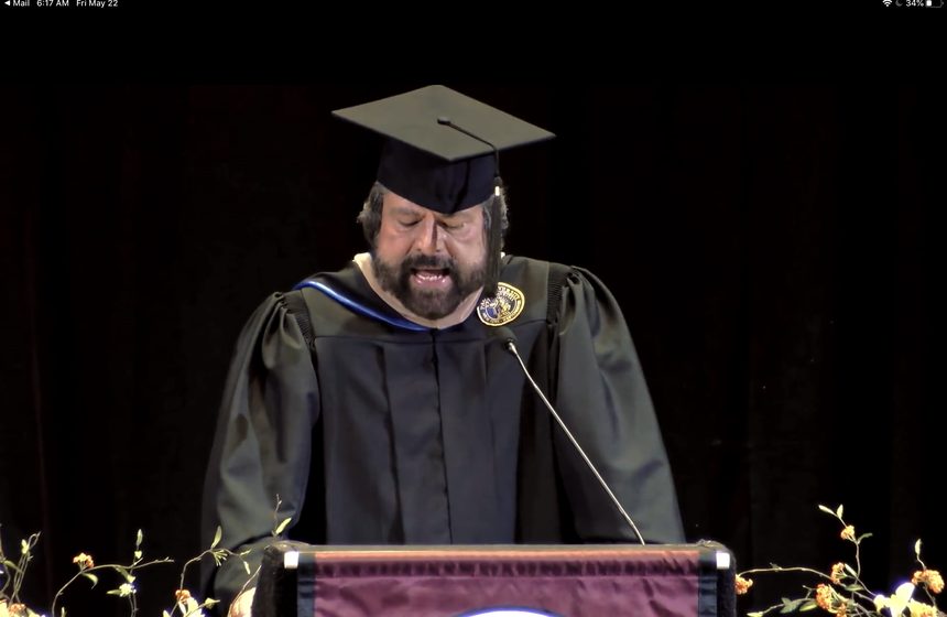Dennis Bonilla in academic cap and gown delivering a college commencement address at the podium