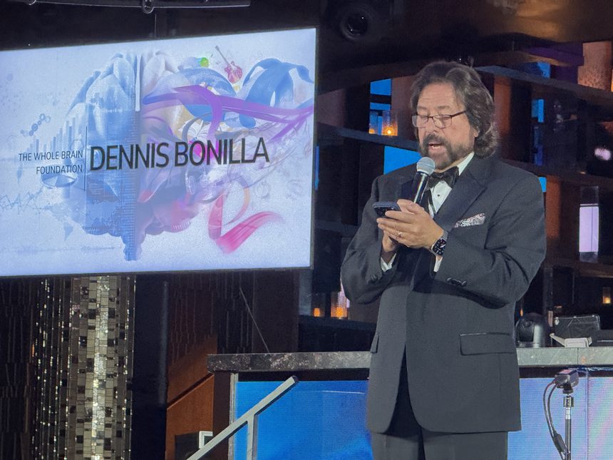 Dennis Bonilla speaking on stage in black tie at a Whole Brain Foundation event