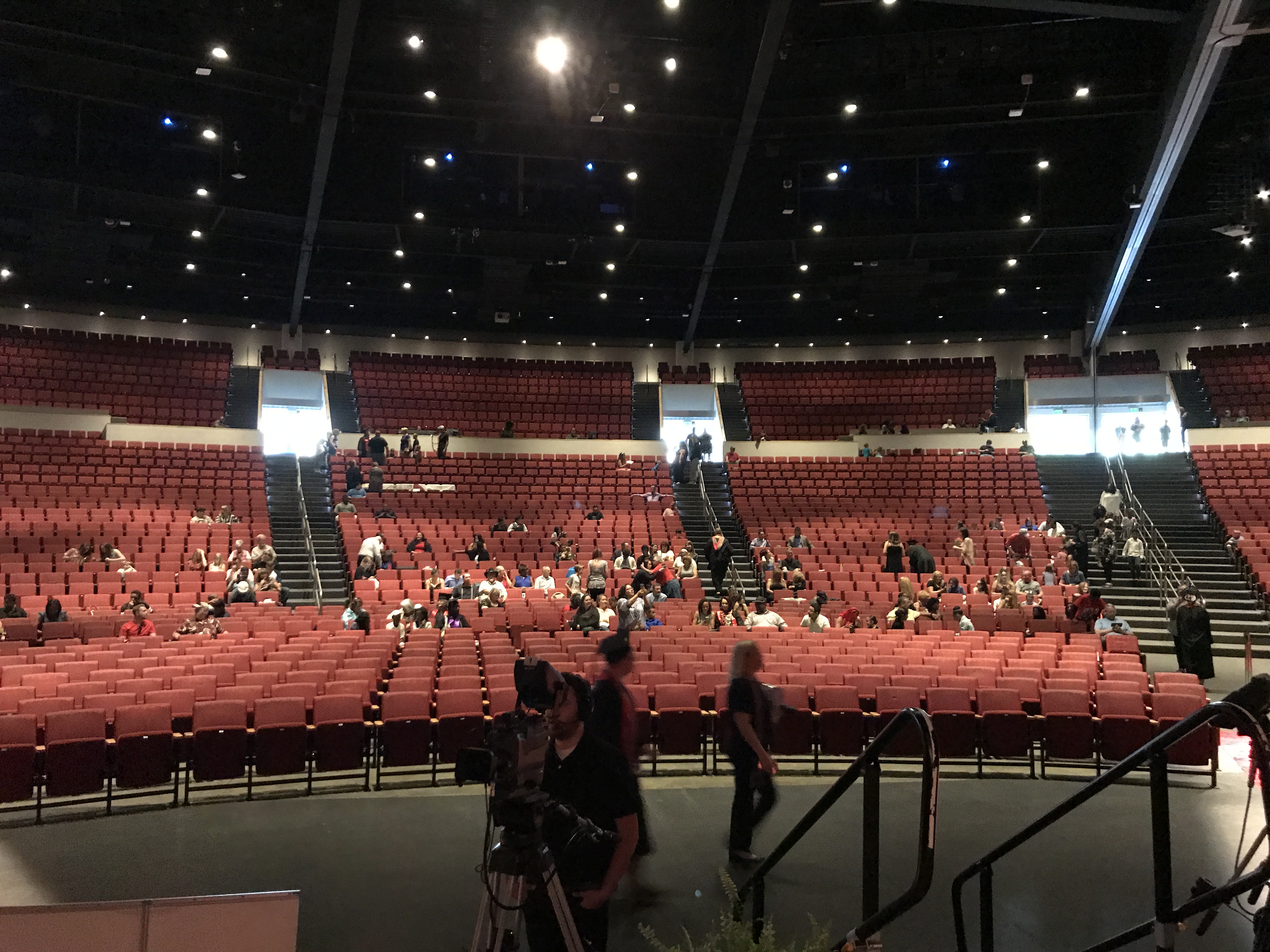 Camera operator filming a university commencement ceremony in a large arena