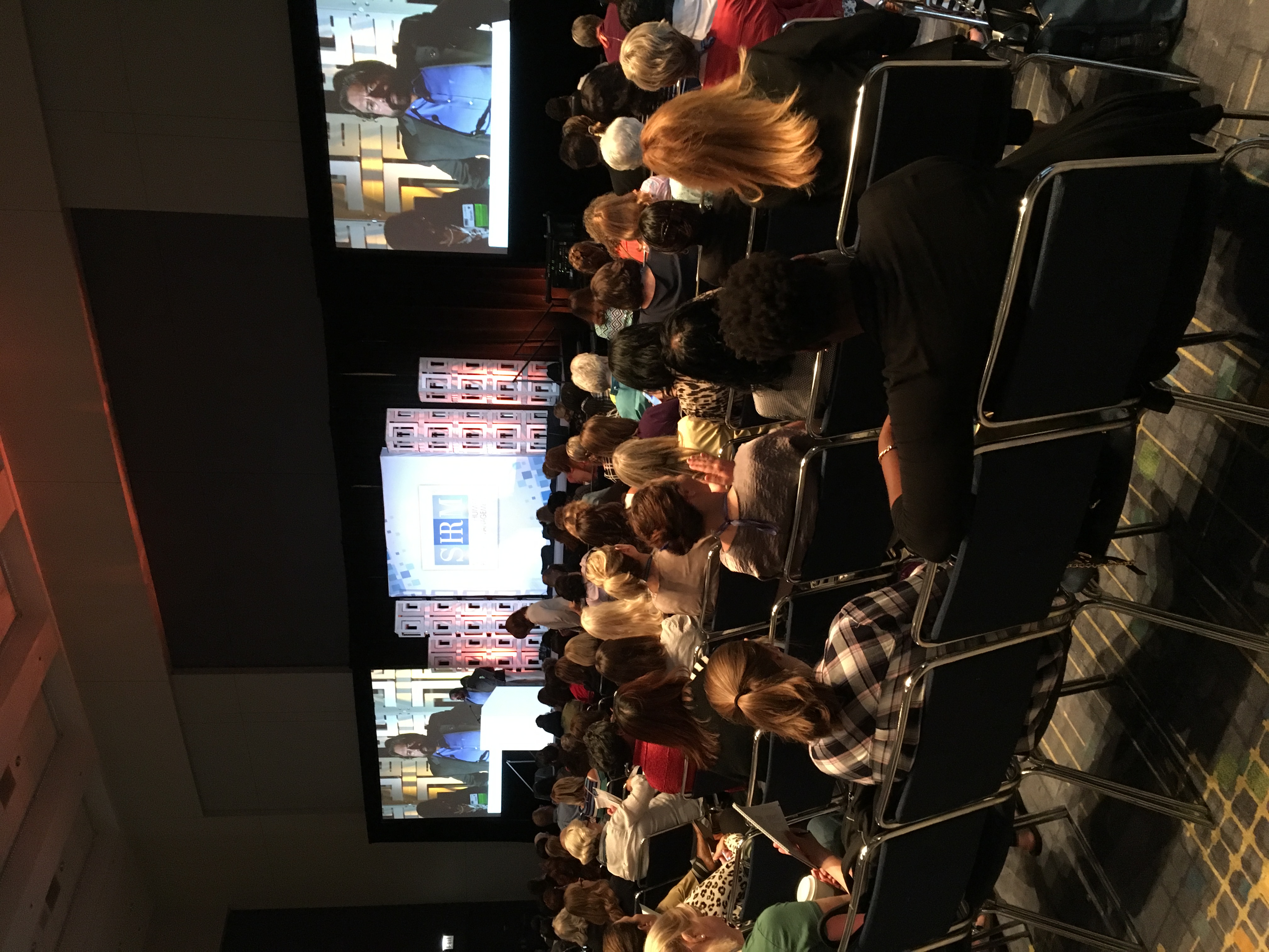 Dennis Bonilla speaking on stage at a SHRM conference with large screens