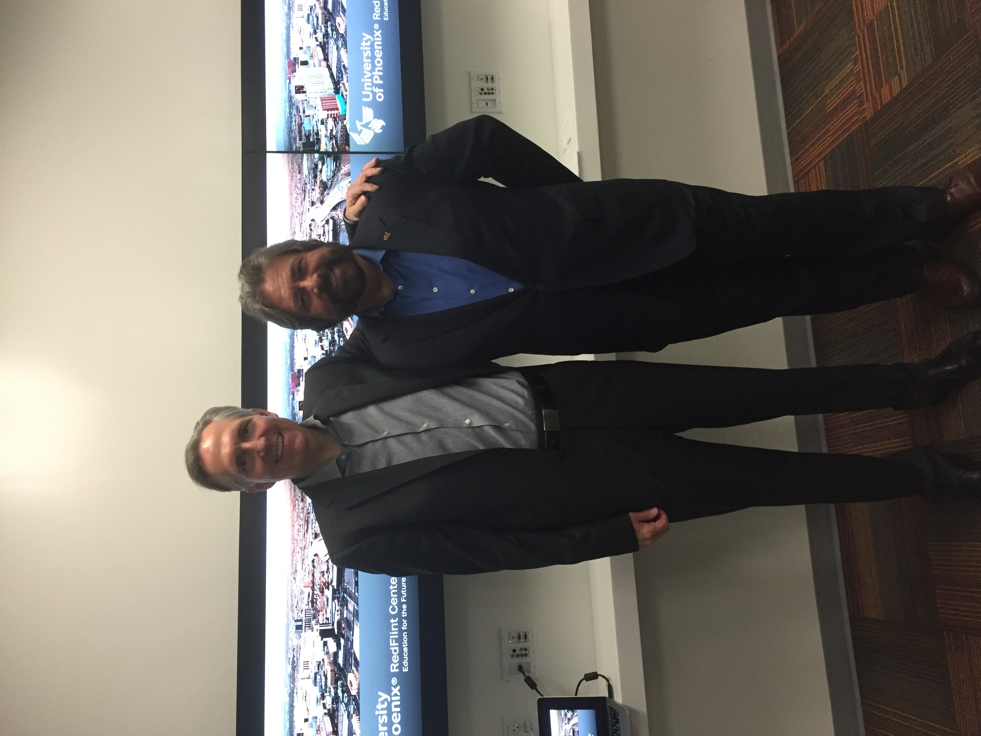 Dennis Bonilla with a colleague in front of a University of Phoenix RedFlint Center display