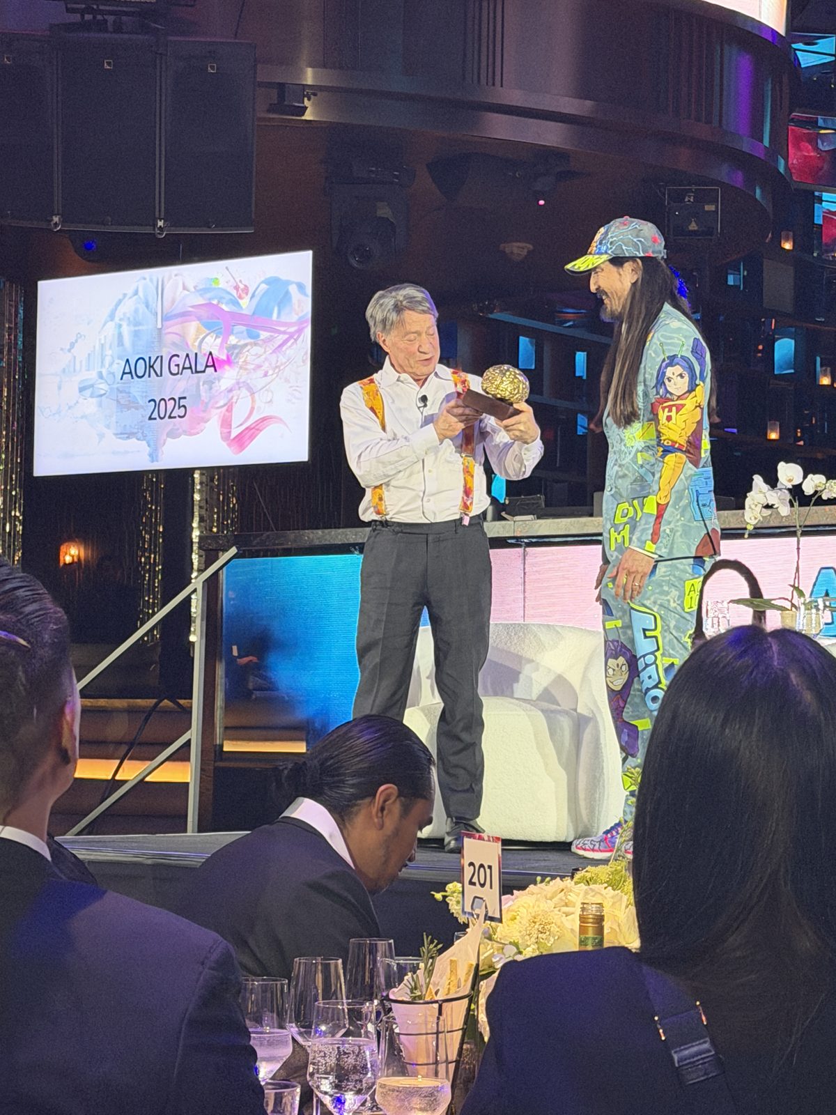 Dennis Bonilla presenting an award to Steve Aoki on stage at the Aoki Gala 2025