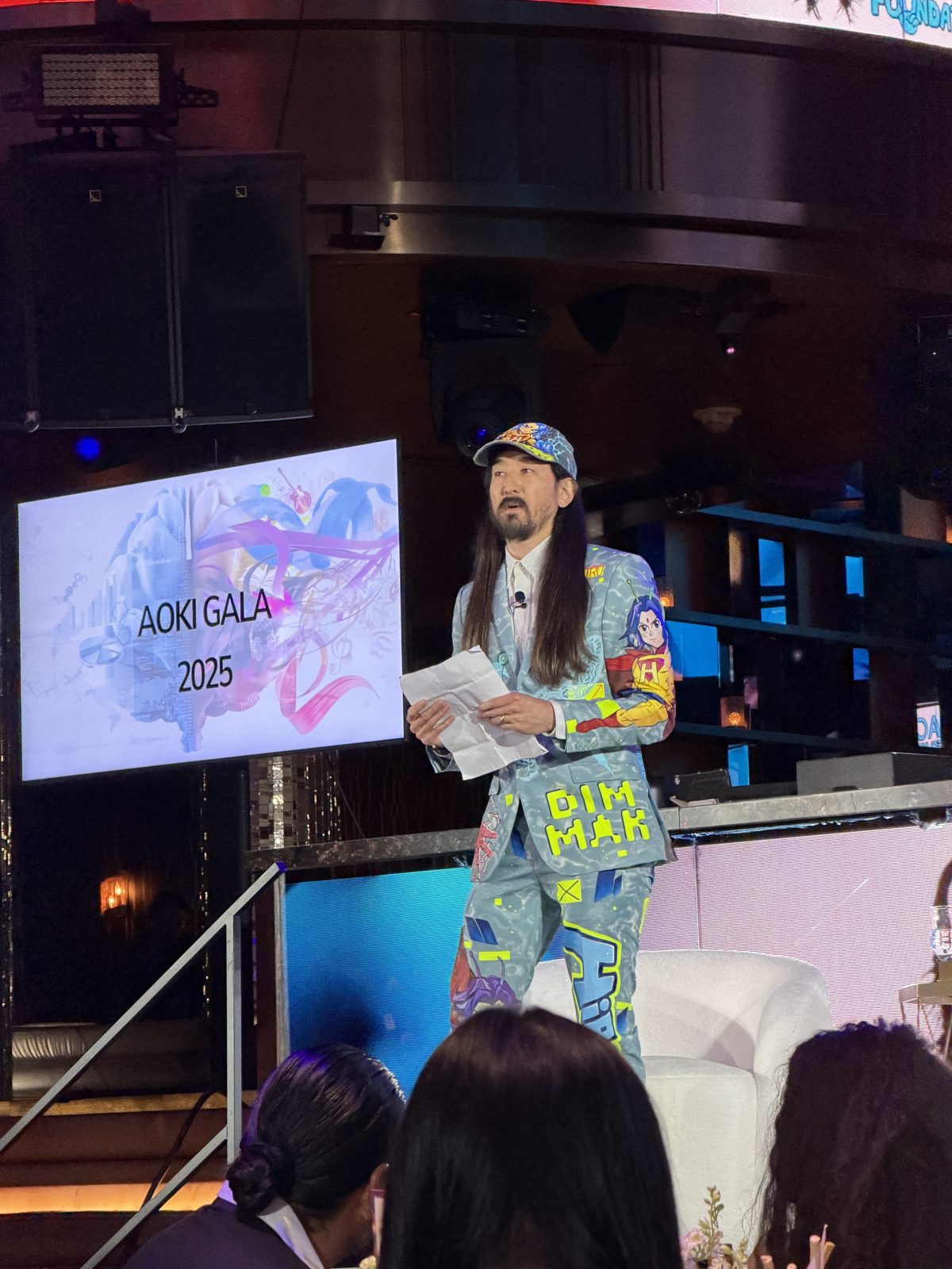 Steve Aoki speaking on stage in front of the Aoki Gala 2025 screen