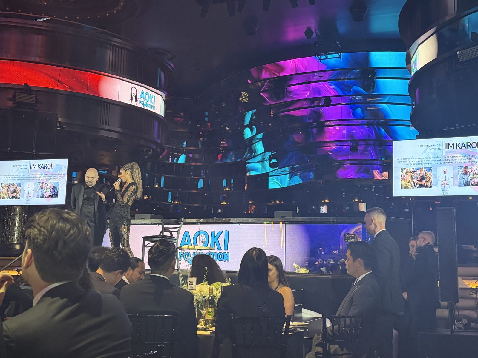 A speaker introducing the Elite Mind/Memory Experience with Jim Karol on stage at the Aoki Gala